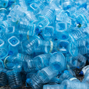 A large pile of empty, crumpled blue plastic bottles stacked on top of each other. The bottles vary in shape and size, with some being more transparent than others. It's a striking scene highlighting plastic waste, reminiscent of the environmental issues the Soneva Charity Foundation aims to address in the Maldives.