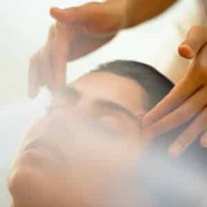 A person with closed eyes receives a gentle facial massage, two hands softly pressing on their temples and forehead. Surrounded by a soft, hazy light, the serene and calming atmosphere feels like one of Soneva's exclusive offers.