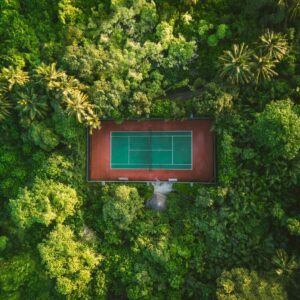 Aerial view of a tennis court with green and blue surfaces, amid dense, lush jungle foliage. Tall trees and various greenery surround the rectangular court at Soneva, creating a striking contrast between the structured sports area and the wild natural environment for an exclusive Maldives experience.