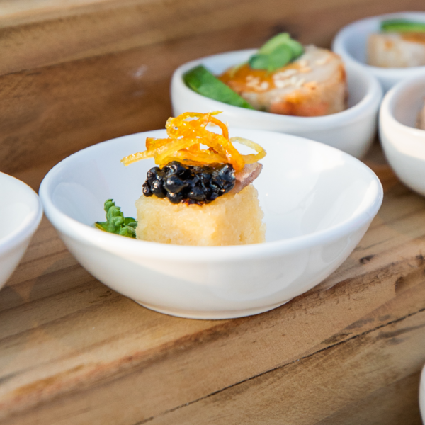An assortment of small, elegant appetizers in white bowls arranged on a wooden surface. The dishes feature garnishes like caviar, orange zest, and various greens, reminiscent of the vibrant presentations seen at Chinese New Year celebrations in the Maldives at Soneva resorts.